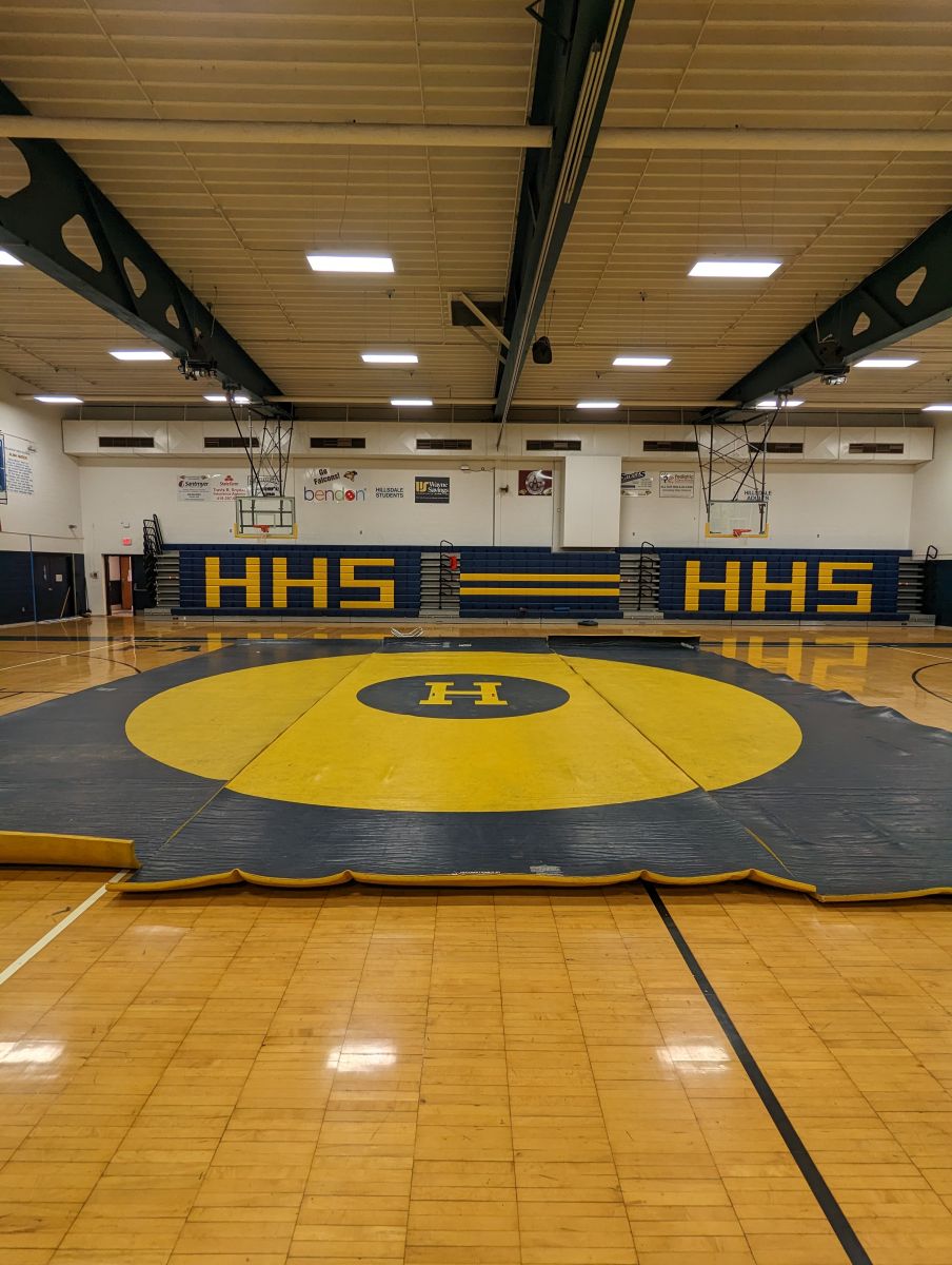 An image of a wrestling mat in blue and gold with the letter "H" in the center.
