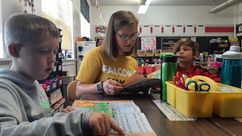 A high school student-athlete reads out loud to a small group of elementary students in their classroom.