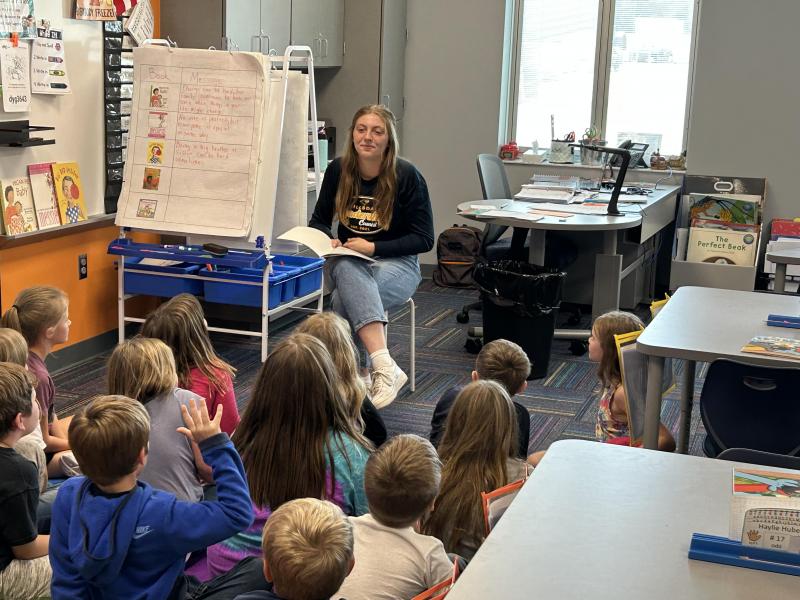 An image of a high school student reading to 2nd graders.