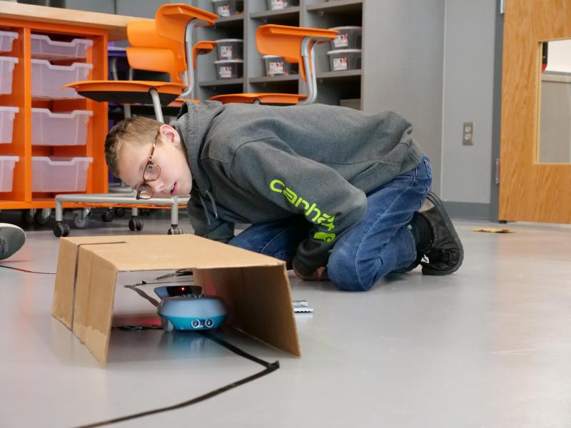 A student watches a finchbot move through a cardboard tunnel.