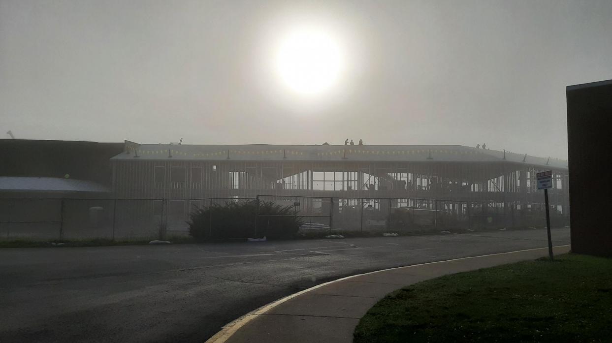In the fog, workers work on the roof of the new educational building under construction.