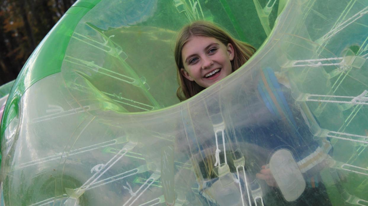 A student stands inside an inflatable bumper ball with her head visible through the open hole at the top.