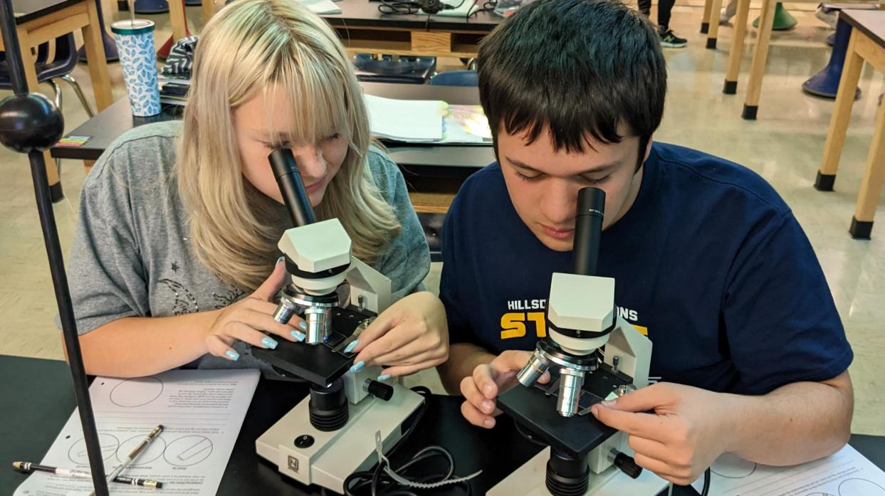Two students examine evidence using microscopes.