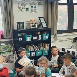 High school students read aloud to elementary students who follow along in copies of their own books.