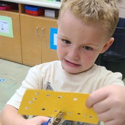 A kindergartener uses a hole punch to punch holes in paper. 