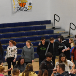 Students stand in a circle, arms entwined, on the gymnasium floor.