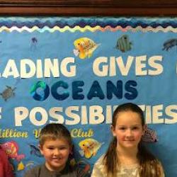 Three students stand in front of a bulletin board with the text: "Reading gives us oceans of possibilities."