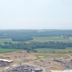 This is an overhead drone photo with trees and others' properties in the foreground, the school construction site in the middle of the photo and others' properties in the background. 