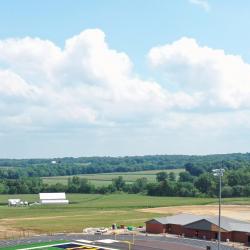  This is a drone shot with the football/soccer field to the left. At the higher parking lot elevation in the foreground, a crane lifts the press box from the flatbed of a truck. In the background center, the new field house at the lower elevation is visible.