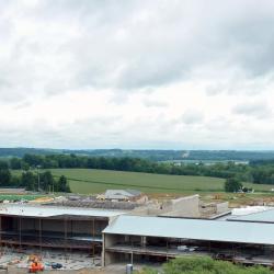 This is a drone shot looking at from a side angle of the new educational building in the background with the existing red brick high school facility to the right and the adjacent parking lot to the left.