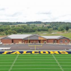 The Falcon head logo is front and center on the football/soccer field with the field house in the background.