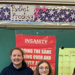Students stand in front of a sign with "Padlet Prodigy" printed on it.