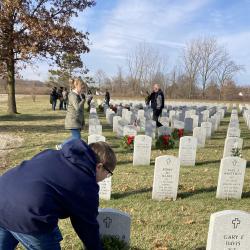 A student places a wreath on the gravesite of a U.S. Military service member.