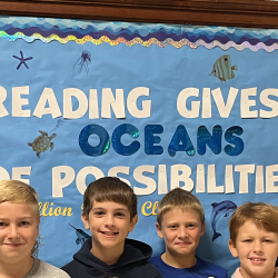 Six students stand in front of a bulletin board with the text: "Reading gives us oceans of possibilities."