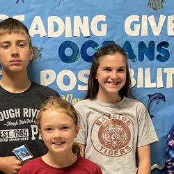 Five students stand in front of a bulletin board with the text: "Reading gives us oceans of possibilities."