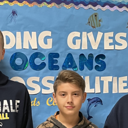 Three students stand in front of a bulletin board with the text: "Reading gives us oceans of possibilities."