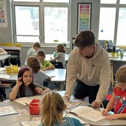 An image of a high school student working with 2nd graders.