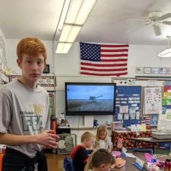 An FFA member stands in the elementary classroom with students working on the craft.