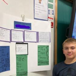 A student stands in front of his group's poster board and holds a sample of their recipe.