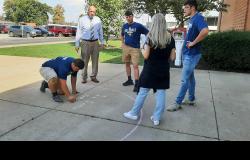 A student writes a math formula with chalk on the sidewalk.