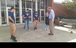 Mr. Mack and students look down at their work on the sidewalk.