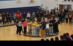 Students stand in a circle, arms entwined, on the gymnasium floor.