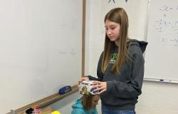 A student holds an unwrapped gift with a partially-filled shoebox in front of her.